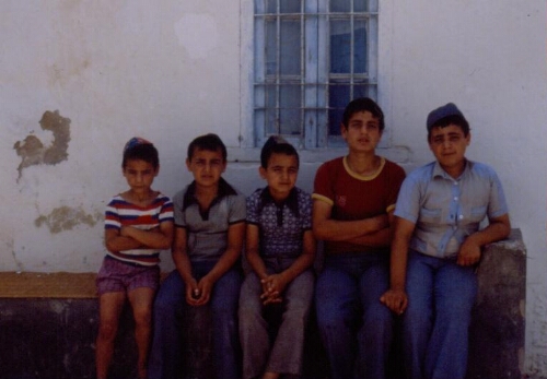 Cinq garçons assis sur un banc à l'extérieure de la synagogue de la Ghriba